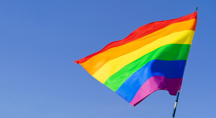Gay rainbow flag waving in the wind in a clear blue sky