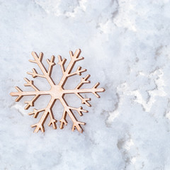 Merry Christmas and Happy New Year greeting card with wooden snowflake on snow background with copy space. Flat lay. Top View.