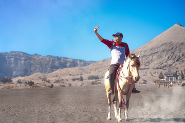 Asian traveller use smartphone selfie on between ride a horse at Bromo mountain