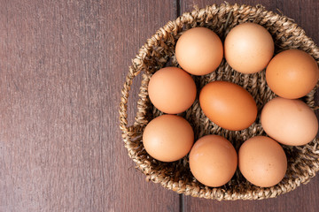 Top view of organic raw chicken eggs in bamboo basket with copy space on brown wooden floor background