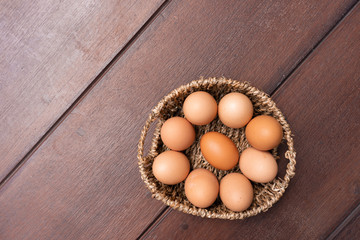 Top view of organic raw chicken eggs in bamboo basket with copy space on brown wooden floor background