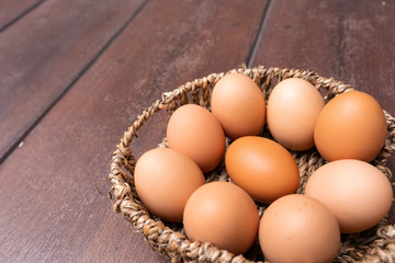 Close up of organic raw chicken eggs in bamboo basket on brown wooden floor background