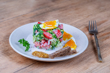 Delicious salad with broccoli, tomato, onion and boiled egg with cream sauce in plate on wooden background. Healthy food