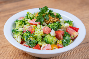 Delicious salad with broccoli, tomato, onion and boiled egg with cream sauce in plate on wooden background. Healthy food