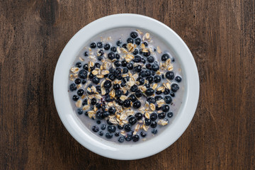 Oatmeal with fresh blueberry, almond milk and honey for breakfast in plate on wooden background. Rustic style. Top view.