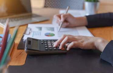 Fototapeta premium Businesswoman working on calculator to calculate business data financial report on wooden table.
