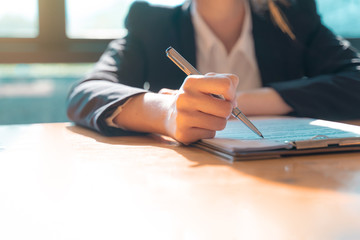 Fototapeta premium Hand of businesswoman sitting at the table and writing on business contract in office.