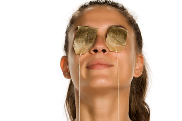 Young smiling woman posing with tea bags on her eyes on white background