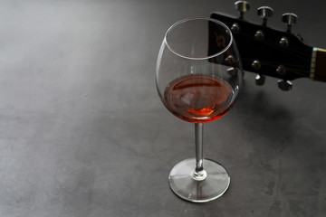 Guitar and high glass with red wine on a stone background.