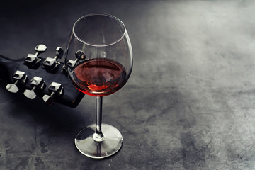 Guitar and high glass with red wine on a stone background.