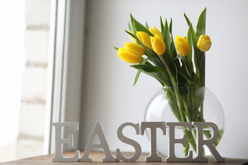 A bouquet of yellow tulips in a vase on the windowsill. A gift to a woman's day from yellow tulip flowers. Beautiful yellow flowers in a vase by window.