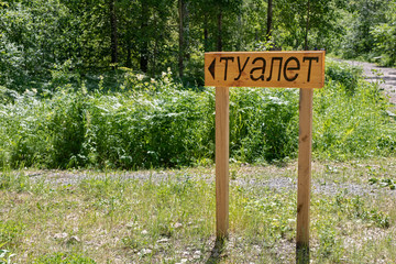 wooden signpost in the forest with the inscription in Russian toilet 
