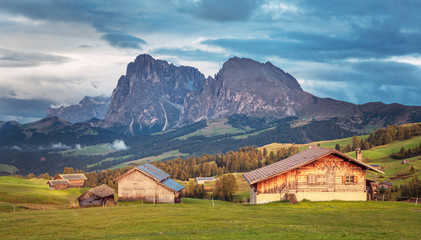 Fototapeta na wymiar Alpe di Siusi - Seiser Alm with Sassolungo - Langkofel mountain group in background at sunset. Wooden chalets in Dolomites, Trentino Alto Adige, South Tyrol, Italy, Europe
