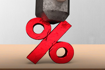 Sledgehammer smashing red percentage sign cracked on wooden table with concrete wall background.