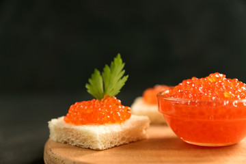 Delicious red caviar on wheat bread served with parseley on wooden desk.