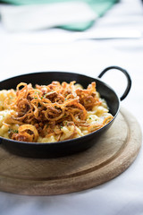 close up of traditional alpine cheese Spätzle in a iron pan served on a wooden board