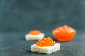 Square shaped sandwich eith red caviar on gray background