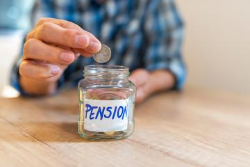 Man hands with coins in glass jar, close up. Responsible investing. Pension. Glass jar with coins and an inscription pension. Man holds coin in his hand