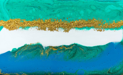 Liquid uneven blue and green marbling pattern with golden glitter and glare of light