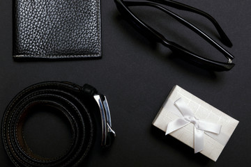 White men's tie and a leather belt with a couple on black background, top view. 