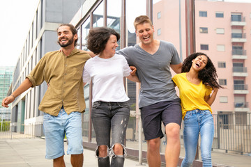 Happy carefree friends walking outside and having fun together. Young men and women hanging out in city, hugging each other, joking and laughing. Friendship and freedom concept