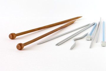 Different types of knitting needles: wooden, metal, plastic, 5 pieces for knitting socks and a curved auxiliary needle for knitting braids on a white background. Close up, space for text