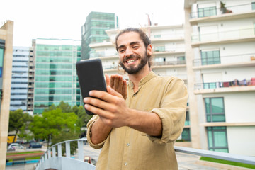 Cheerful happy hipster guy blowing kiss to phone screen. Young man in casual talking through video call on mobile phone. Communication concept