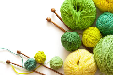 Crafts and Hobbies. Green and yellow balls of yarn for hand knitting and wooden needles on a white...