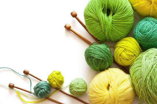 Crafts and Hobbies. Green and yellow balls of yarn for hand knitting and wooden needles on a white background. Empty space for text. Flat lay, close up, macro