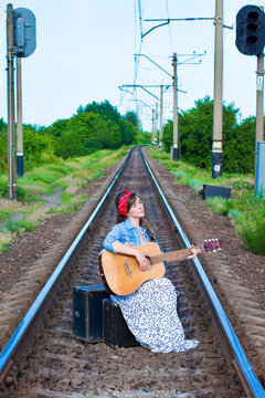 A beautiful girl plays the guitar. Pretty woman with old suitcases on the train tracksl. A teenager in a denim jacket, a long dress and a red bandage.