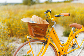 Vintage travel concept. Photo of a yellow bicycle with hat in basket, standing in field