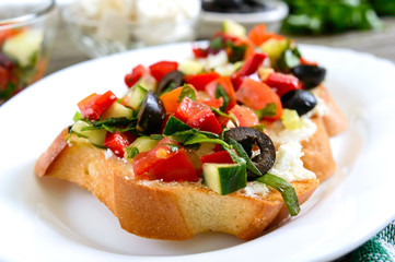 Classic bruschetta with tomatoes and feta on a white plate on a wooden background. Italian sandwiches with toasted baguette, goat cheese, fresh vegetables, basil.