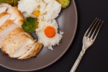 Baked chicken breasts or fillet on plate with rice and vegetables on plate.