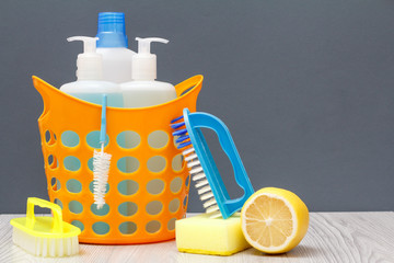 Bottles of dishwashing liquid in a basket with brush on wooden desk.