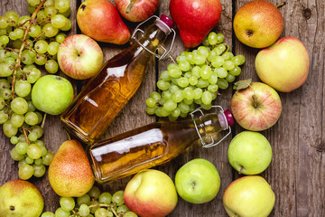 Homemade Apple Cider Vinegar Flatlay of Fresh Ripe Apples Pears and Green Grapes Two Bottles of Apple Juice or Tasty Cider Top View Wooden Background Horizontal
