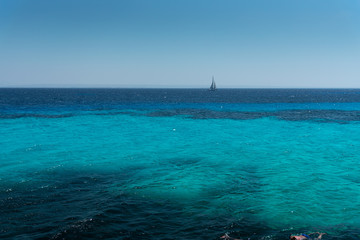 The sea in front of the island Favignana, with a boat sailing and the coastline of Sicily in the background