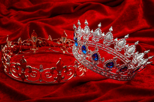 Royal authority, monarchy and ruling class concept with princess or queen silver crown with decorative sapphire gems and a king gold crowns with diamond gemstones isolated on red velvet background