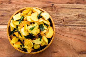 Deep fried spicy cassava chips in a wooden bowl on a table, isolated.