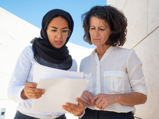 Muslim professional explaining to colleague document details. Arab and Caucasian business women...