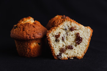 Muffins with raisins and one muffin cut in half on black background