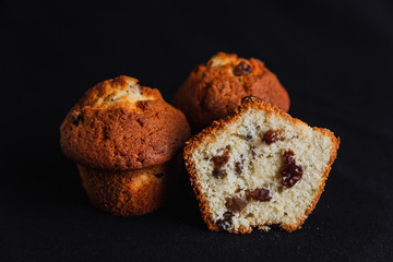 Muffins with raisins and one muffin cut in half on black background