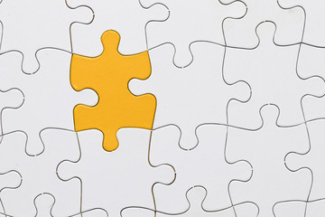 Fototapeta premium White jigsaw puzzle sheet with yellow puzzle piece in center