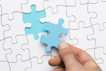 Elevated view of hand holding blue puzzle piece over white puzzle background