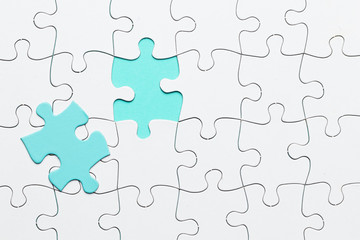 Fototapeta premium Turquoise piece of puzzle on white jigsaw puzzle backdrop
