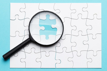 High angle view of magnifying glass on missing puzzle over blue background