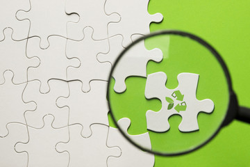 Magnifying mass on white puzzle with recycle icon over green surface