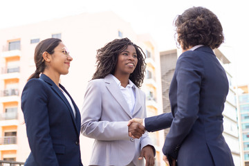 Smiling employees shaking hands on street. Cropped shot of young multiethnic businesswomen meeting outdoor. Business concept