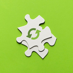 Elevated view of recycling icon on white puzzle piece over green backdrop