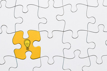 Fototapeta premium Idea icon on yellow puzzle piece connected with white grid puzzle backdrop