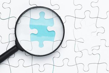 Elevated view of magnifying glass on missing puzzle piece on grid